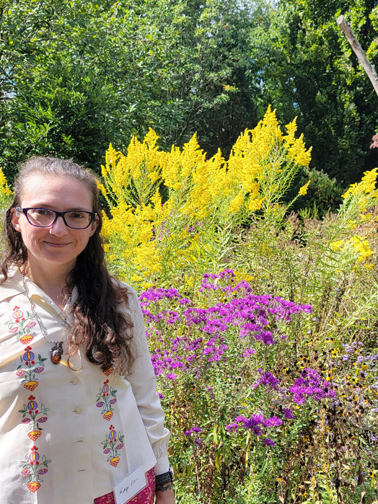 Magi standing in front of a community planting of goldenrod, vernonia, black-eyed susans and blue mistflowers