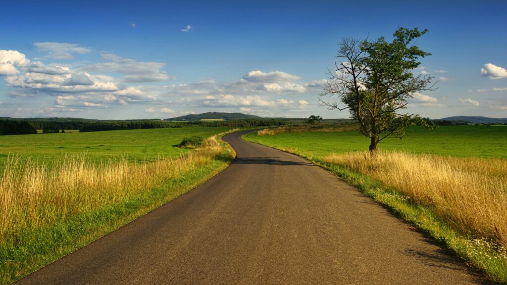 Scenic view of a winding road through peaceful countryside fields with blue skies.