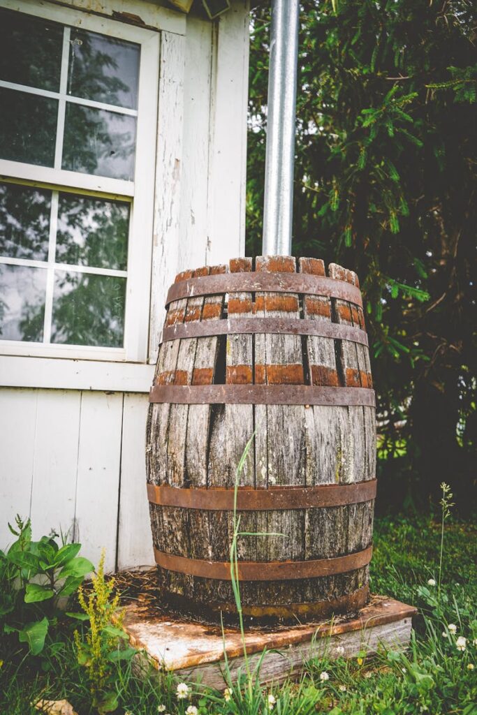 Vintage wooden barrel with metal bands beside a garden shed, surrounded by greenery. Sustainability involves thinking how we can repurpose old objects in new ways